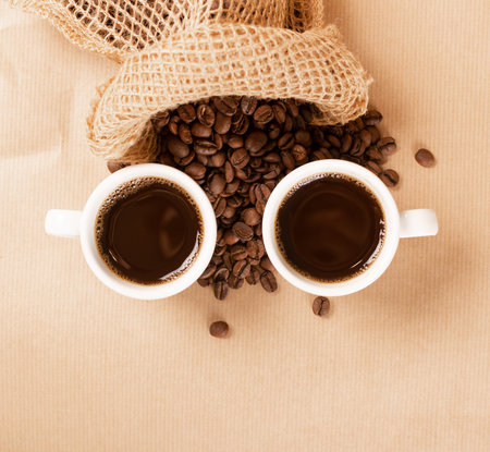 Hot coffee cup and coffee beans on brown background top view with copy space. White coffeecup or mug...