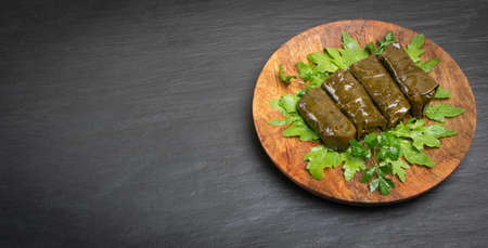 Macro Photo of Traditional Turkish Dolma, Sarma or Dolmades on Wooden Plate. Mediterranean Dish Dolmadakia or Tolma Stuffed Grapes Leaves on Black Stone Background with Copyspaceの写真素材
