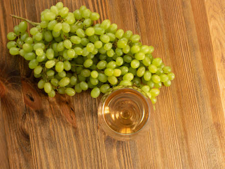 White wine glass on ripe bunch of grapes background in sunny day. Wineglass with golden grape sparkling drink on wooden rustic winery table top viewの写真素材