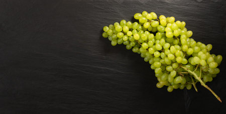 Bunch of sweet green seedless grapes on black stone background with copyspace. Ripe grape on dark...