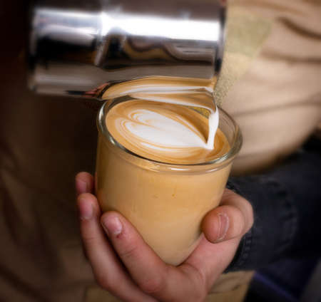 Male hands preparing latte or cappuccino art in coffeeshop closeup. Barista makes coffee with milk in coffee shop cafe close upの写真素材