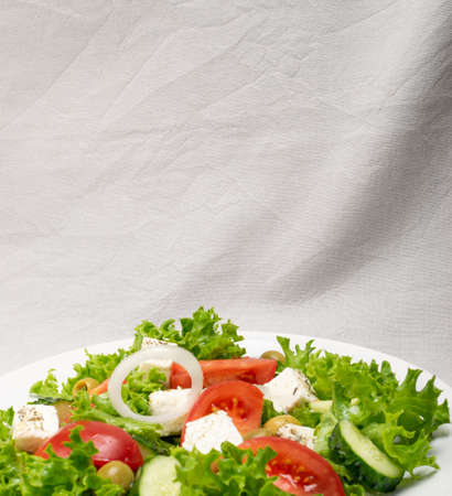 Greek salad or horiatiki with large pieces of tomatoes, cucumbers, onion, feta cheese and olives in white bowl closeup. Green village salad with diced mozzarella, lettuce, spices and olive oilの写真素材