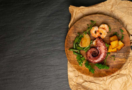 Traditional greek grilled seafood on restaurant wooden plate served with shrimps and vegetables rustic style. Delicious barbecue octopus tentacle with fresh greens top view, copyspaceの写真素材