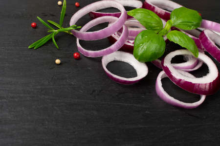 Fresh sliced red onion on black background with copy space. Raw purple onion rings or shallot slices with greens and spicesの写真素材