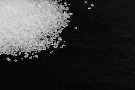 Big sugar crystals on black background close up. Macro shot of sucrose crystals, sea salt rock or granulated sodium salt texture on food slate with selective focusの写真素材