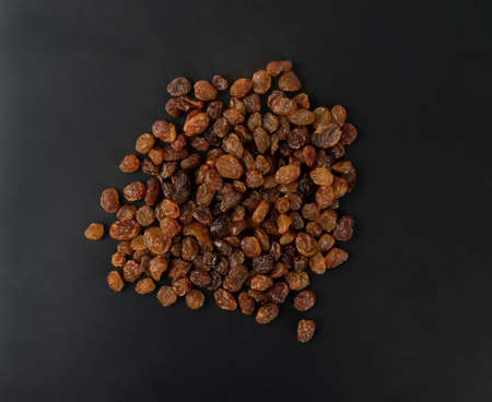 Heap of sweet raisins on black background. Dried grapes pile, handful of dark brown raisin top view flat layの写真素材