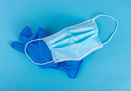 Medical mask and used medical gloves on blue background. Surgical masks cover mouth and nose. Disposable medic clothing item, hospital equipment, corona virus face protection conceptの写真素材