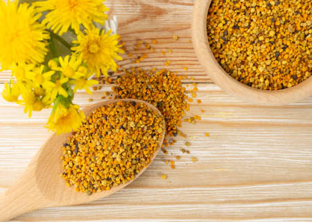 Macro shot of bee pollen or perga in wooden spoon on blurred rustic background. Raw brown, yellow, orange and blue flower pollen grains or bee bread. Healthy food supplement with selective focusの写真素材