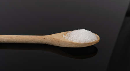 Heap of White Powder of Baking Soda, Clay or Bentonite in Wooden Spoon on Black Background. Powdered Citrus Acid, Calcium, Gypsum or Plaster Side Viewの写真素材