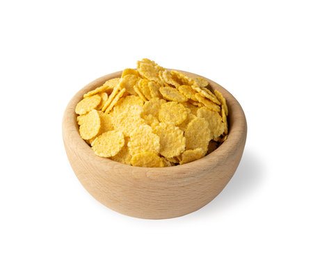 Yellow corn cereal for breakfast in round wooden bowl isolated on white background. Pile of crispy...