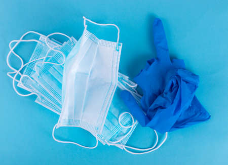 Medical mask and used medical gloves as if showing the middle finger on blue background. Surgical masks, disposable medic clothing item, hospital equipment, virus face protection conceptの写真素材