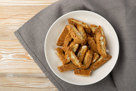 Biscotti di prato on rustic tablecloth burlap background. Traditional italian cantuccini nuts cookies. Homemade cantucci shortbread with almond on white plate top viewの写真素材