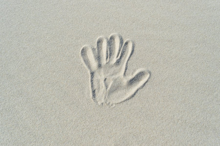 One hand print on white sand texture. Hand print on sandy beach background top view with copy spaceの写真素材