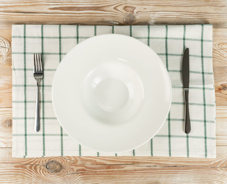 Empty white plate and cutlery on wooden table top view with copy space. Rustically kitchen mock up...