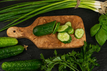 Sliced cucumber with green vegetables on rustic cutting board. Fresh cucumbers, green onion or spring chive, basil and parsley ready for saladの写真素材