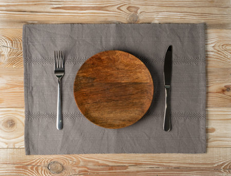 Empty wood plate and cutlery on wooden table top view with copy space. Rustically kitchen mock up...