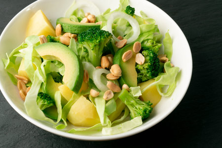 Green salad with avocado, cucumber, broccoli, potatoes and peanuts on white restaurant plate....