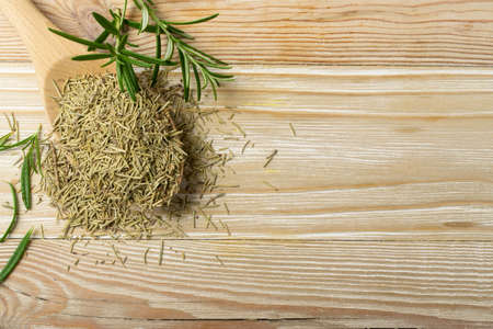 Pile of dry rosemary needles in a wooden spoon. Dried crushed and fresh green rosemary leaves top view. Ground seasoning, herbs and spices on wood backgroundの写真素材