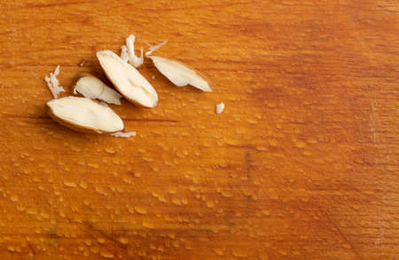 Crushed almonds on wooden cutting board closeup. Sliced scattered almond seeds and cut kernels collectionの写真素材