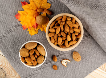 Heap of almond in wooden bowl on rustic background. Scattered almonds with shell and peeled nuts top...