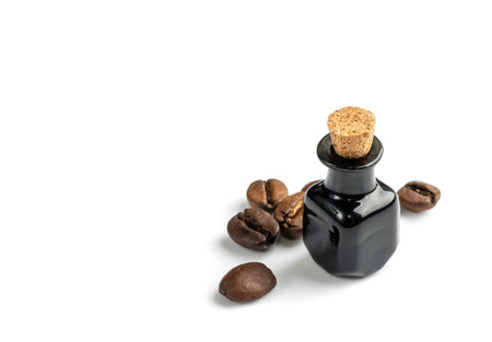 Macro photo of coffee beans oil in small vintage bottle isolated. Organic essential oil of whole roasted coffea arabica, tincture, extract, infusion closeupの写真素材