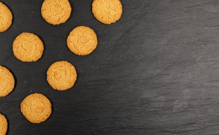 Thin oatmeal cookies mockup. Healthy cereal oat crackers top view on black background. Crispy anzac...