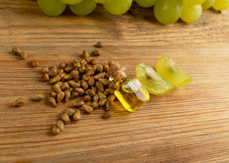 Grape oil seed in small vintage bottle. Heap of grape seeds with green slices and cold press organic essential oil, tincture, extract, infusion on wooden rustic background closeupの写真素材