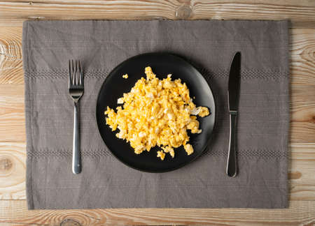 Scrambled eggs or omelet on black plate and cutlery on wooden table top view with copy space. Rustical kitchen mock up with morning hot omelette, fresh omletの写真素材