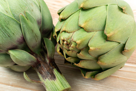 Macro shot of fresh artichoke on wood background. Two whole green artichokes closeup, raw edible cynara flower buds close upの写真素材