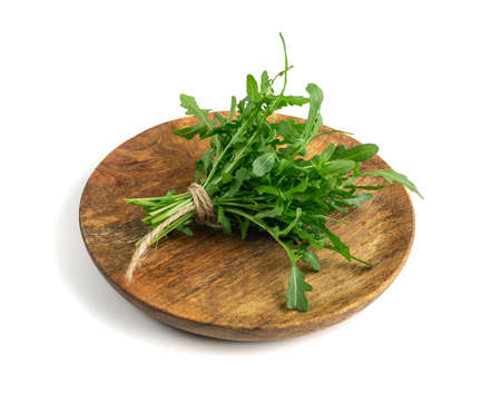 Arugula bunch on wooden plate isolated. Fresh arugula, ruccola leaves, rucola, eruca or garden roquette saladの写真素材