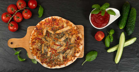 Whole Round Pizza on Dark Stone Background with Fresh Vegetables and Greens Top Viewの写真素材