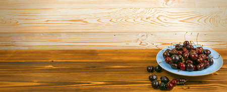 Round blue plate of fresh ripe cherries on old wooden background for design montage. Vintage wood table desk board with overripe cherries or sweet berries pile close up with copy spaceの写真素材