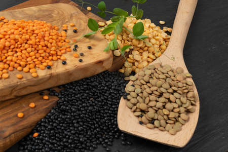 Brown, orange, black lentils and dry yellow peas. Legumes grains mix, dal, raw daal, dhal, masoor collection on black stone backgroundの写真素材