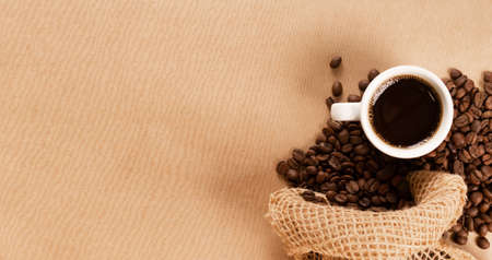 Hot coffee cup and coffee beans on brown background top view with copy space. White coffeecup or mug with black beverage topview with place for textの写真素材