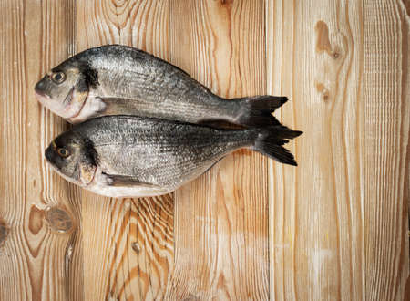 Orata fish on wood background. Fresh dorado, seabream, raw gilt-head bream, dorada, uncooked dorade, doraden or sparus aurata sea fish top viewの写真素材