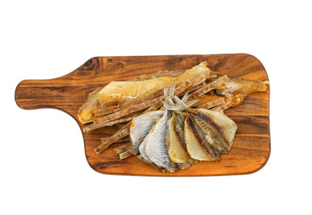 Dried fish mix on wood cutting board isolated. Dry salted seafood snacks, yellowstripe scad, hake...