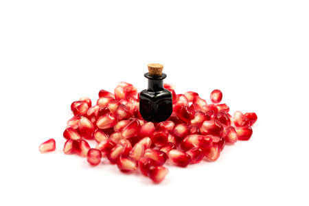 Pomegranate oil with scattered pomegranate seeds isolated on white background. Red punica granatum essential oil, tincture, extract, infusion, volatile oils, essenceの写真素材