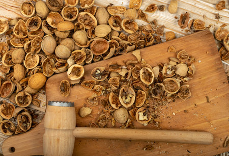Cracking nuts with a hammer on a cutting board top view. Crushed walnuts, empty broken walnut...