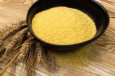 Couscous pile in black bowl. Dry cuscus, raw kuskus, uncooked cous cous or semolina granules on wooden rustic backgroundの写真素材