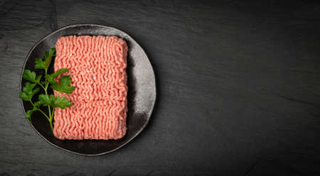 Turkey mince meat mockup. Ground fillet on black background with copy space, uncooked turkey mincemeat flat lay, raw forcemeat, fresh farce meat portion with greens top viewの写真素材