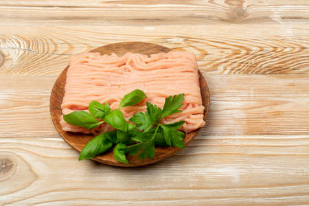 Minced chicken meat on wood background. Ground fresh fillet, uncooked chicken mincemeat, raw poultry forcemeat, farce minced meat portion with greens top viewの写真素材