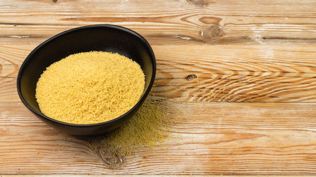Couscous pile in black bowl top view. Dry cuscus, raw kuskus, uncooked cous cous or semolina granules on wooden rustic background with copy spaceの写真素材