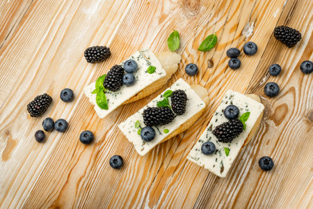 Blue cheese on bread. Gorgonzola with berries and honey, bruschetta with ricotta, blueberries and blackberries, french toasts on wooden rustic background top viewの写真素材