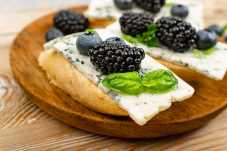Blue cheese on bread. Gorgonzola with berries and honey, bruschetta with ricotta, macro blueberries and blackberries, french toasts on wooden rustic background closeup, selective focusの写真素材