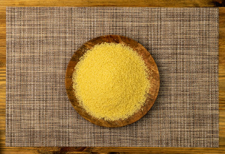 Couscous pile on wood plate top view. Dry cuscus, raw kuskus, uncooked cous cous or semolina granules on wooden rustic backgroundの写真素材