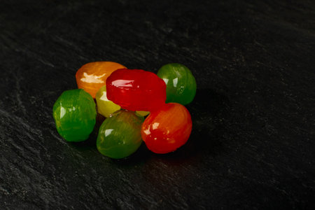 Colorful hard candies pile. Small shiny lollipop pile, fruit confectionery group, round sweets candies on black slate backgroundの写真素材