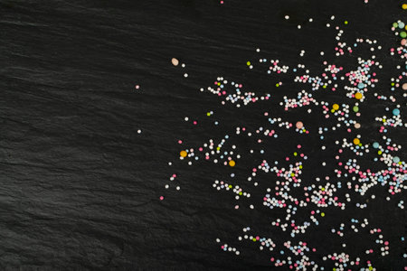 Sweet sprinkles scattered on black background top view. Sweet glaze decoration mix with copy spaceの写真素材