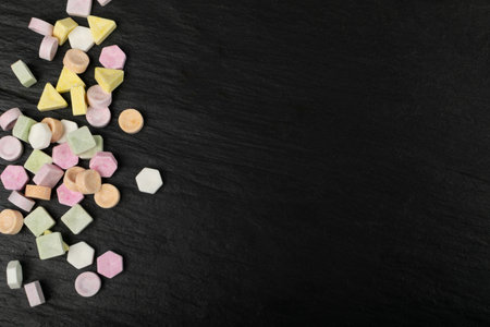 Scattered tablet candies on black stone. Compressed sugar powder confectionery, dextrose candy necklace parts with copy space, vitamin c tablets, lozenges top viewの写真素材