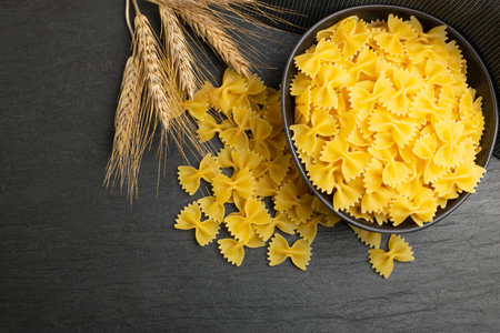 Raw Farfalle Pasta in Bowl, Yellow Dry Butterfly Noodles, Wheat Bow Macaroni, Uncooked Farfalle Pile...