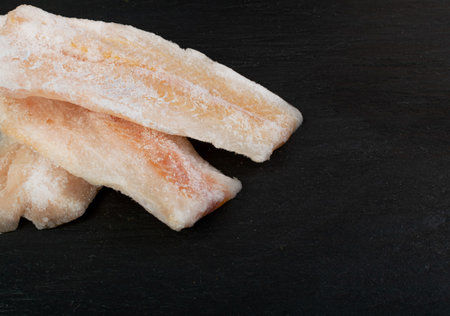 Frozen Fish on Black Plate, White Cod Fillet, Iced Hake Filet, Frozen Pollock Meat on Dark...